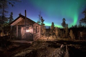 Wooden house in forest during Aurora Borealis